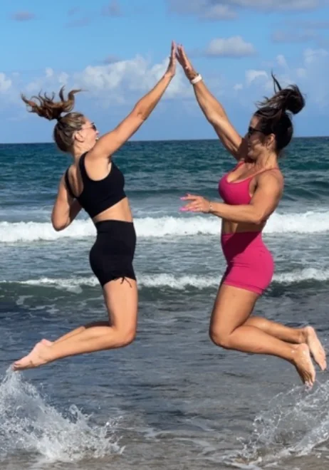 Amanda Ferreira and a client jumping and high-fiving in the surf after a session